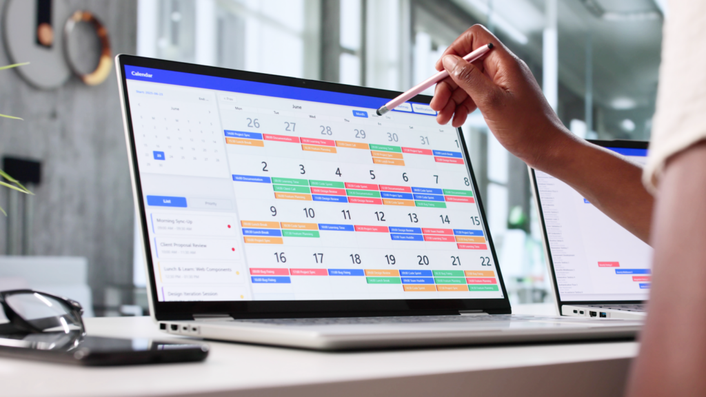A person uses a stylus to scroll through a digital calendar on a laptop.