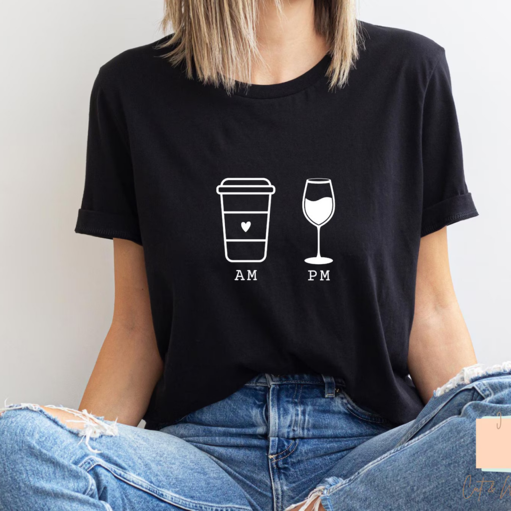 A woman wearing a black t-shirt with white graphics: a coffee cup labeled "AM" and a wine glass labeled "PM".