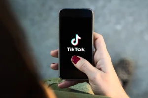 A hand with red nail polish holds a smartphone displaying the TikTok logo on the screen.