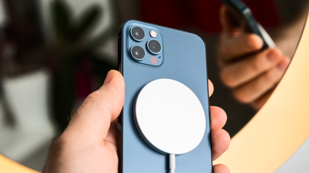 A hand holds a blue smartphone with a circular wireless magnetic charger attached to the back.