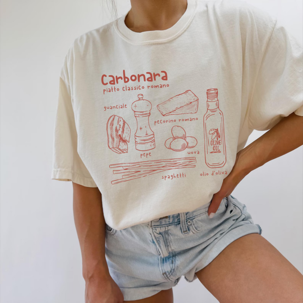 A woman wearing a white t-shirt with red illustrations and text detailing a carbonara recipe with ingredients.