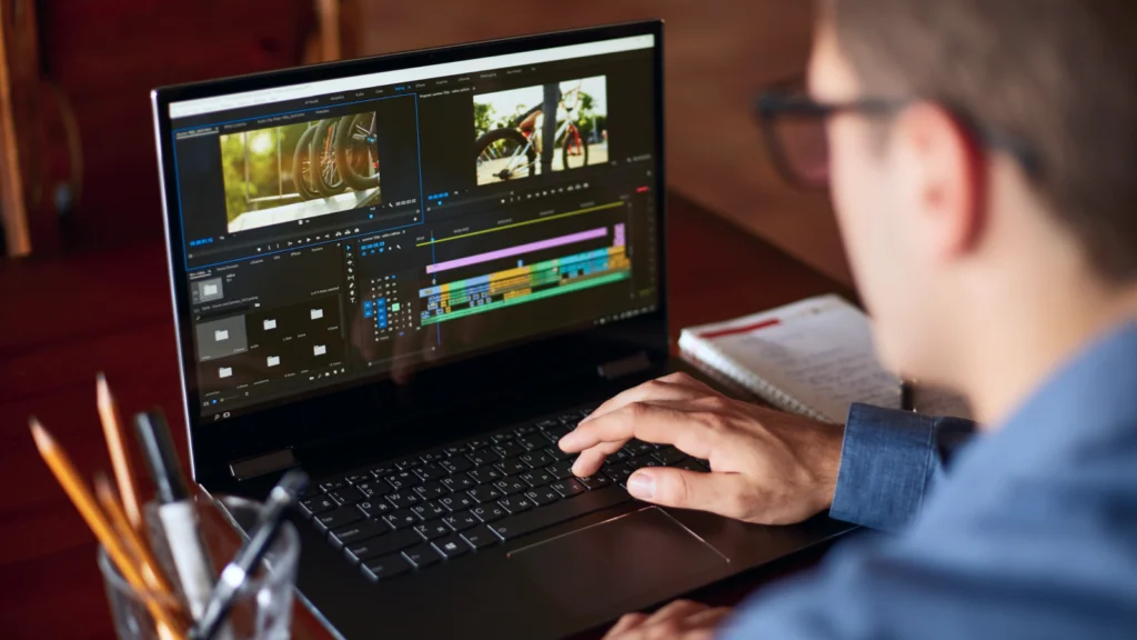 Start a faceless YouTube channel with AI A person edits a video on a laptop, with colorful timelines and clips visible on the screen. The desk has pencils and a notebook.