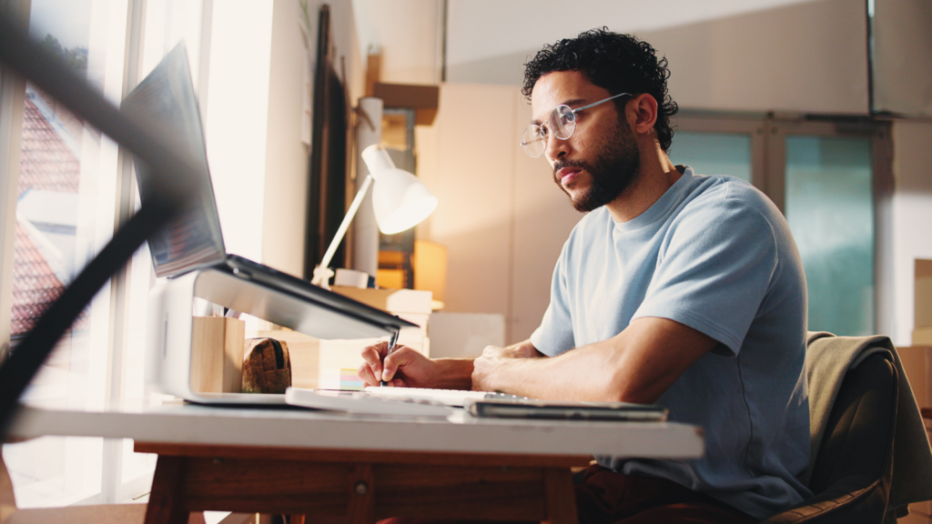 A man in glasses and a light shirt is focused on a laptop, taking notes on the best Wix SEO practices.