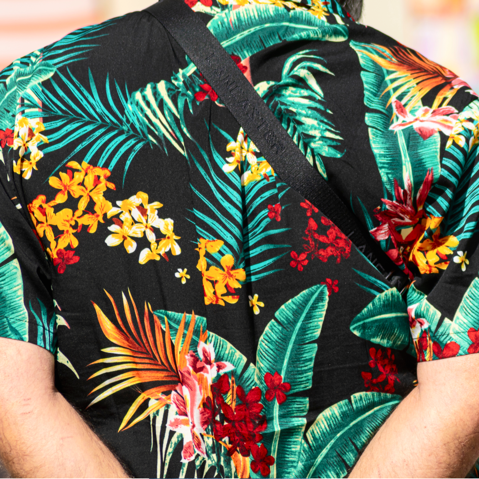A person wearing a vibrant tropical shirt featuring colorful flowers and green leaves on a black background.