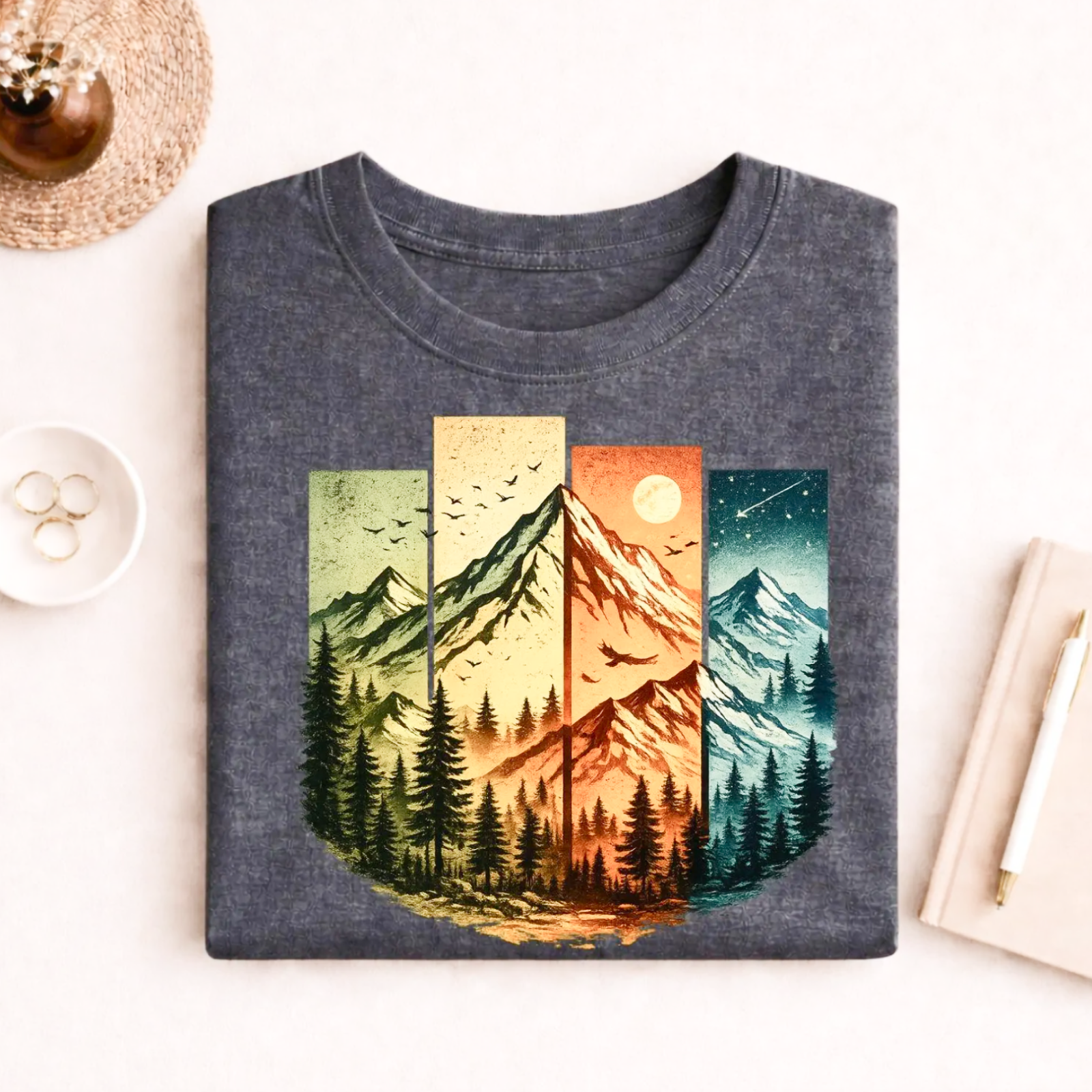 Folded gray T-shirt with a graphic of mountains in four panels, each showing a different time of day.