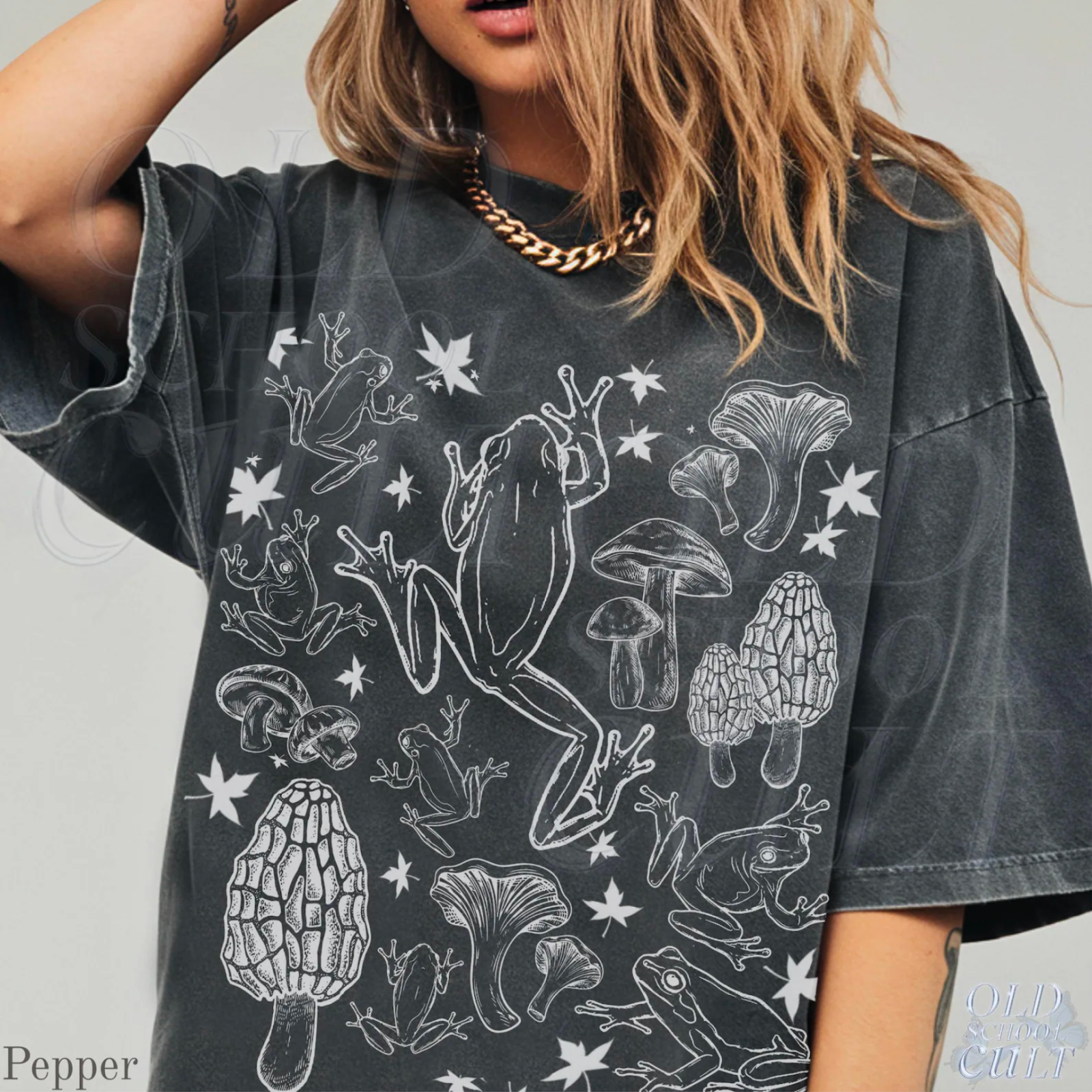 A person wearing a loose, dark gray shirt with white illustrations of frogs and mushrooms.