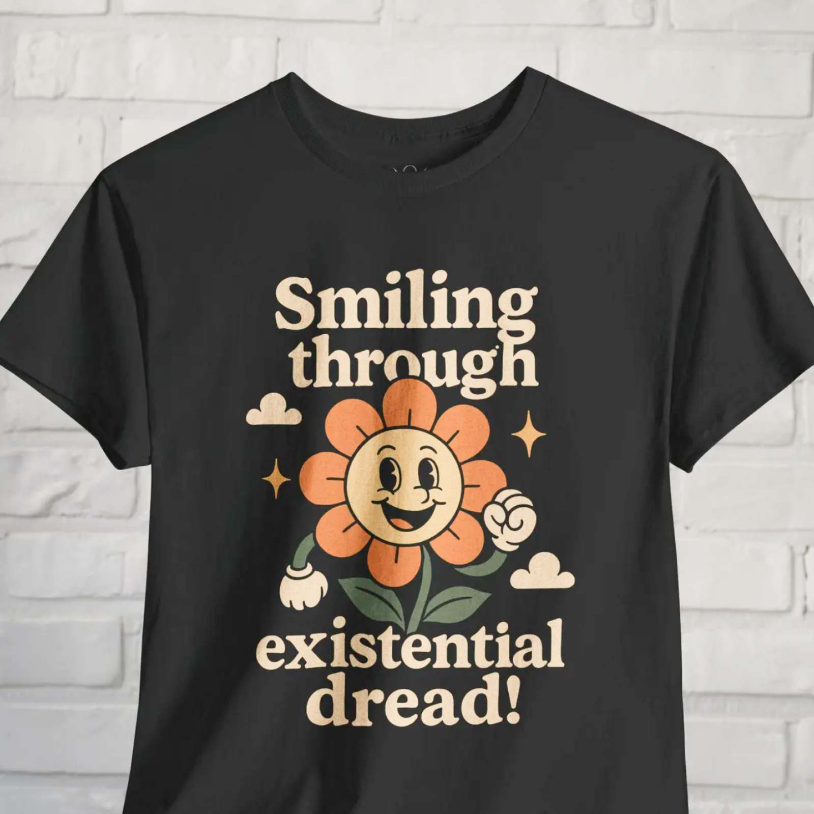 Black T-shirt with a smiling cartoon flower, orange petals, and text: "Smiling through existential dread!"