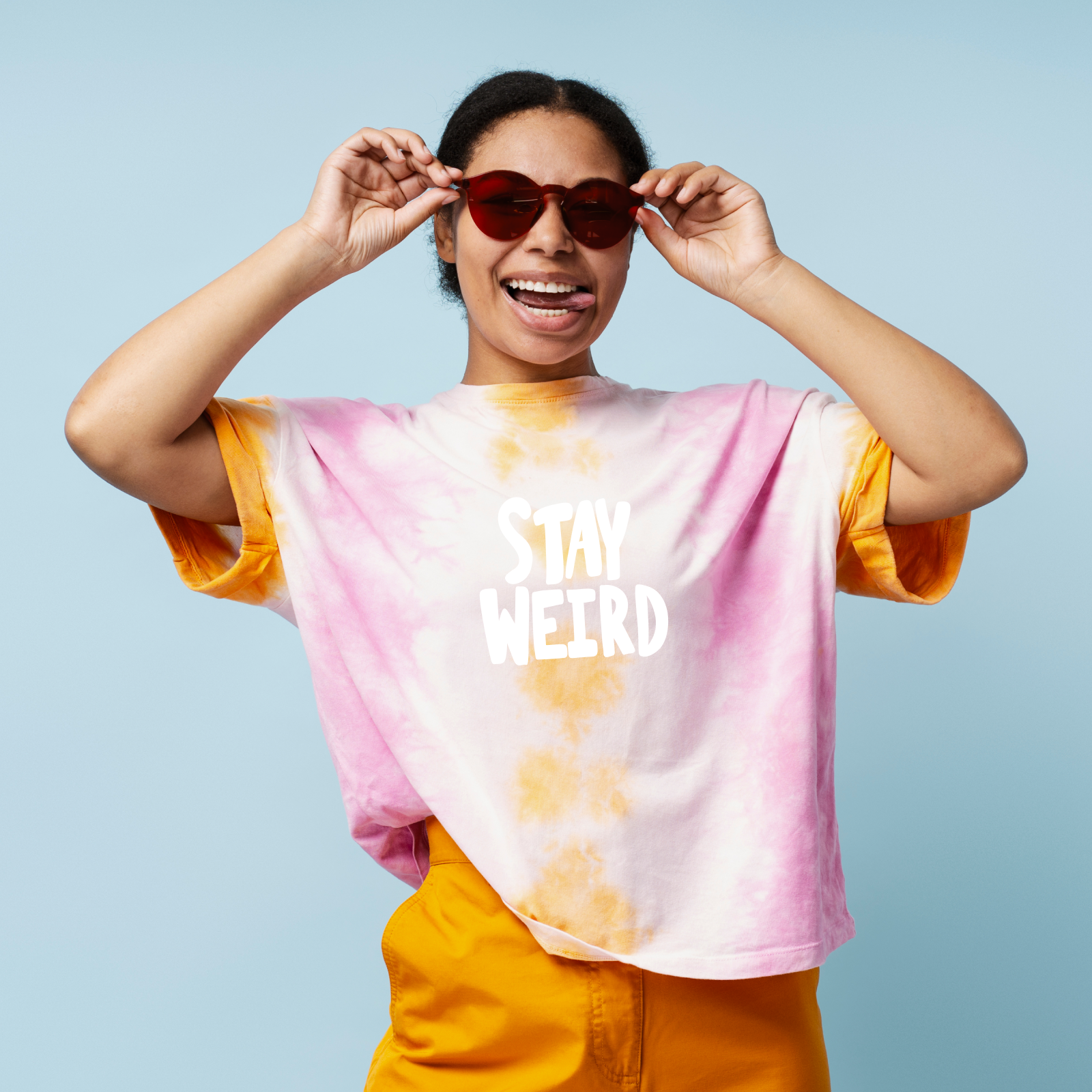 Smiling person in sunglasses and a colorful tie-dye shirt with "Stay Weird" text, posing playfully against a light blue background.