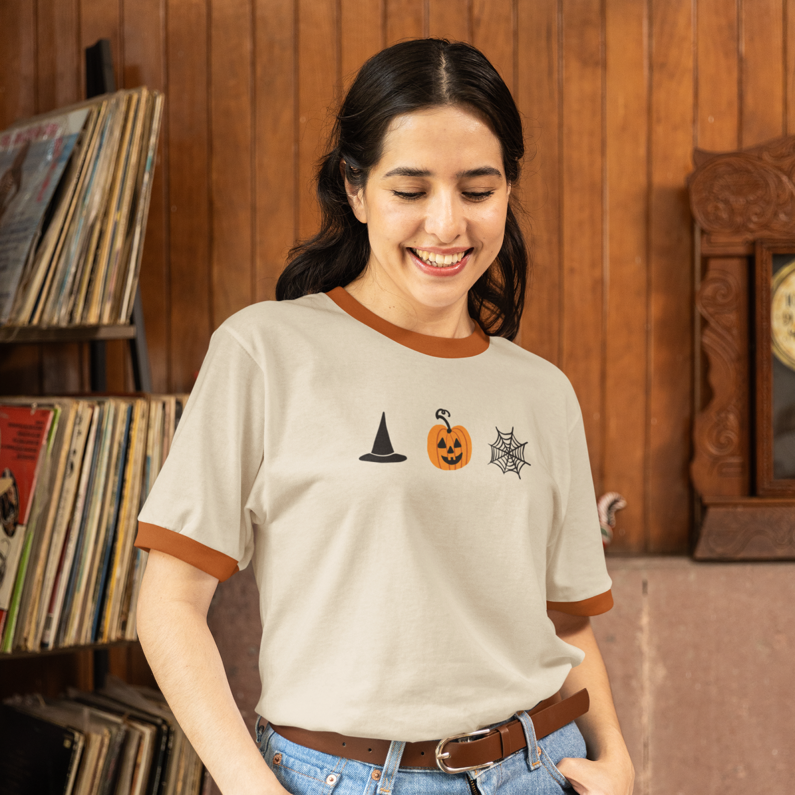 Smiling person wearing a Halloween-themed T-shirt with witch hat, pumpkin, and spider web icons.