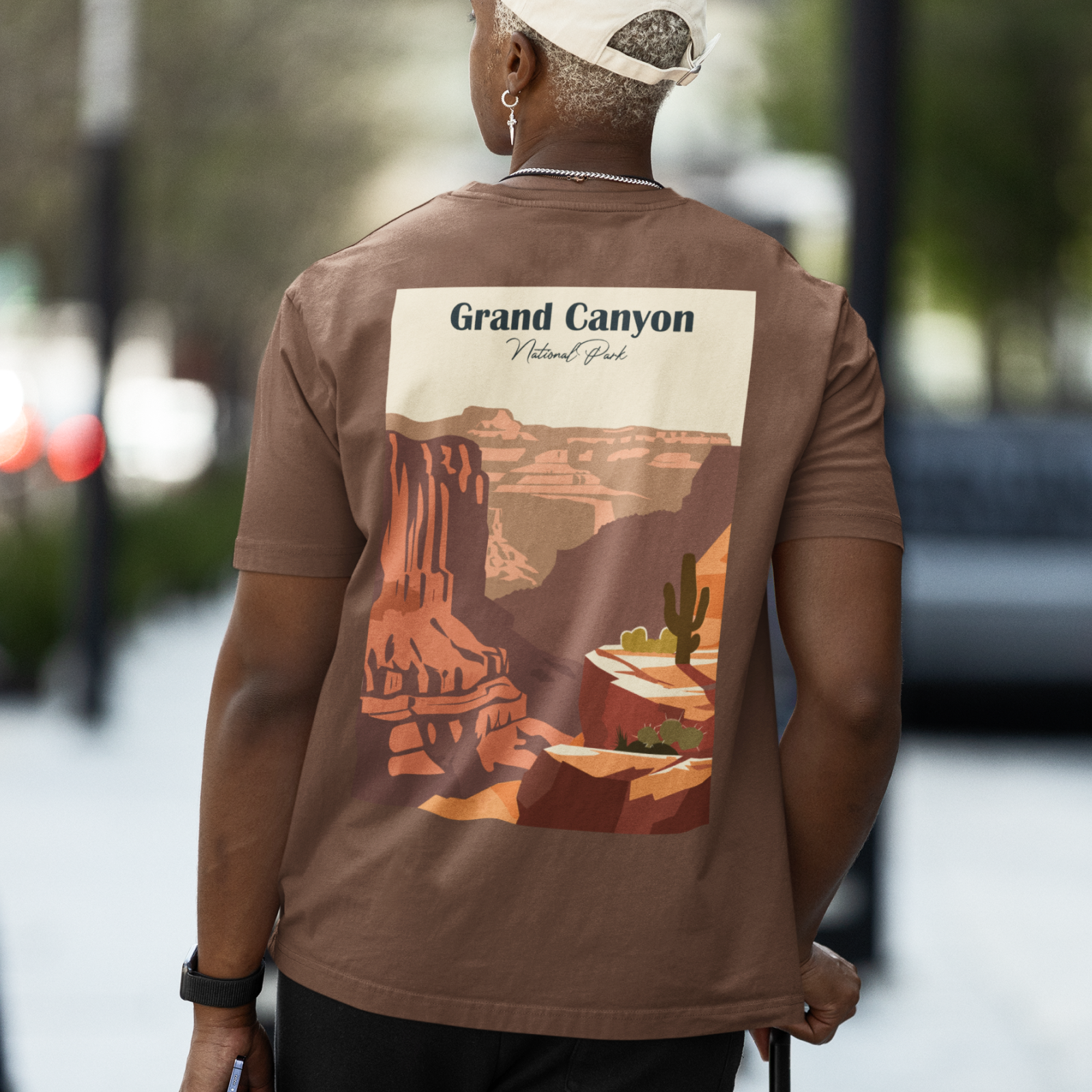A person wearing a brown T-shirt with a vintage-style Grand Canyon print.