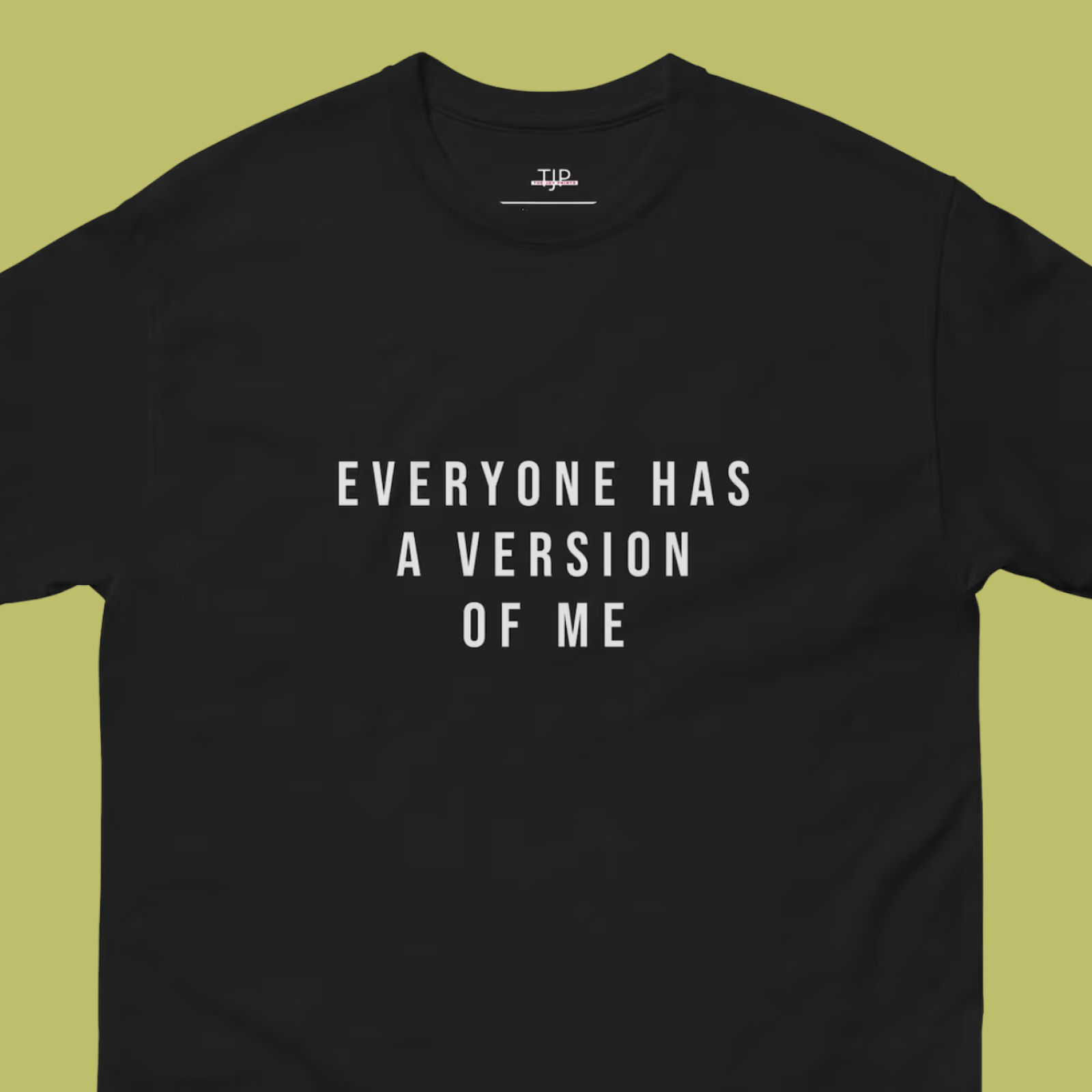 Black T-shirt on a green background with bold white text reading, "EVERYONE HAS A VERSION OF ME," conveying a thought-provoking message.