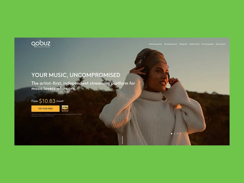 Woman in a cozy sweater enjoys music with headphones against a sunset backdrop.