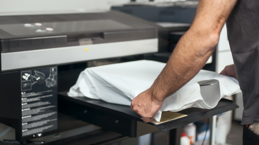 A person places a white t-shirt into a large DTG printing machine, preparing for printing.