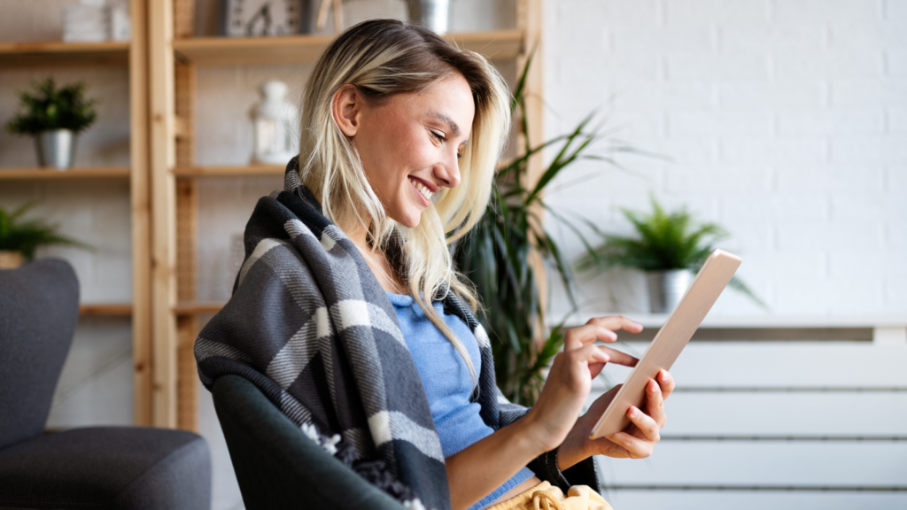 01 Ways to sell Print on Demand with Amazon A smiling woman is wrapped in a blanket, looking at a tablet in her hand.