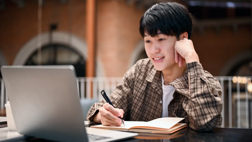 Commission rate strategy for POD A young man is sitting in front of a laptop, with an open notebook where he makes notes on TikTok affiliate marketing.