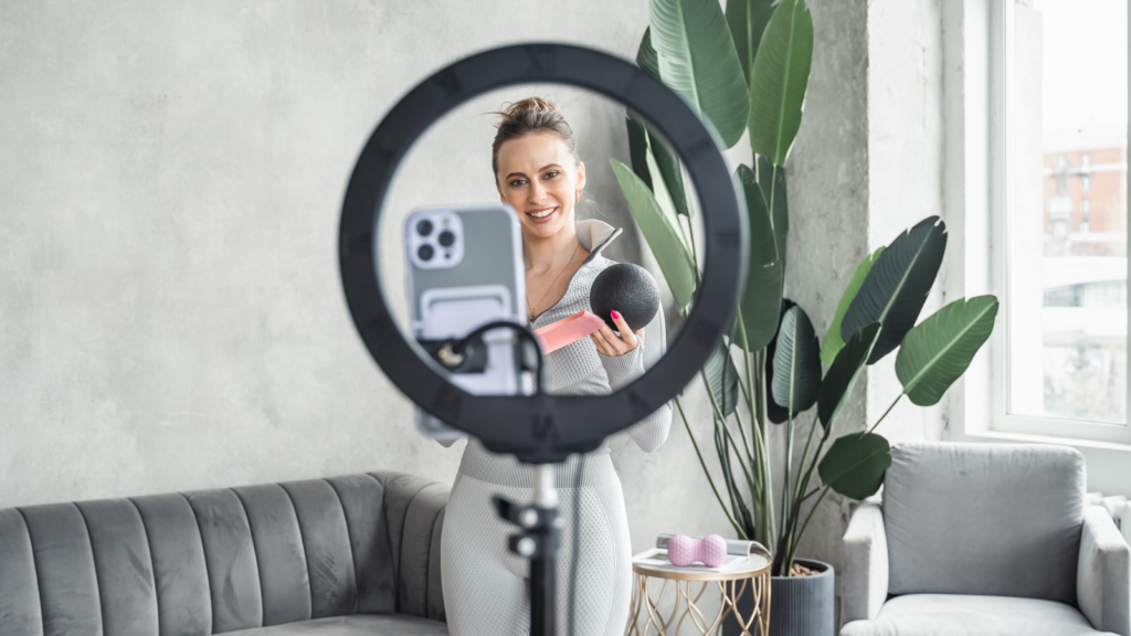 How to gain followers on TikTok A woman in a cozy living room records a fitness vlog. Holding a pink water bottle and a black exercise ball.