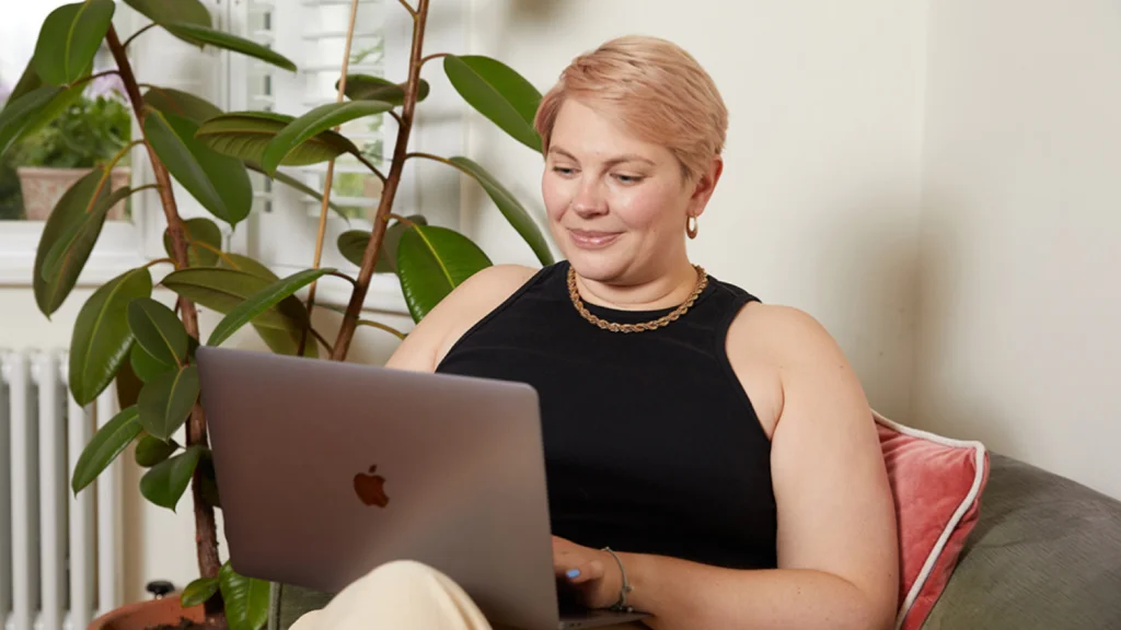 Key TikTok metrics for print on demand sellers A young woman with short hair sits in a chair with a laptop, checking different TikTok metrics.