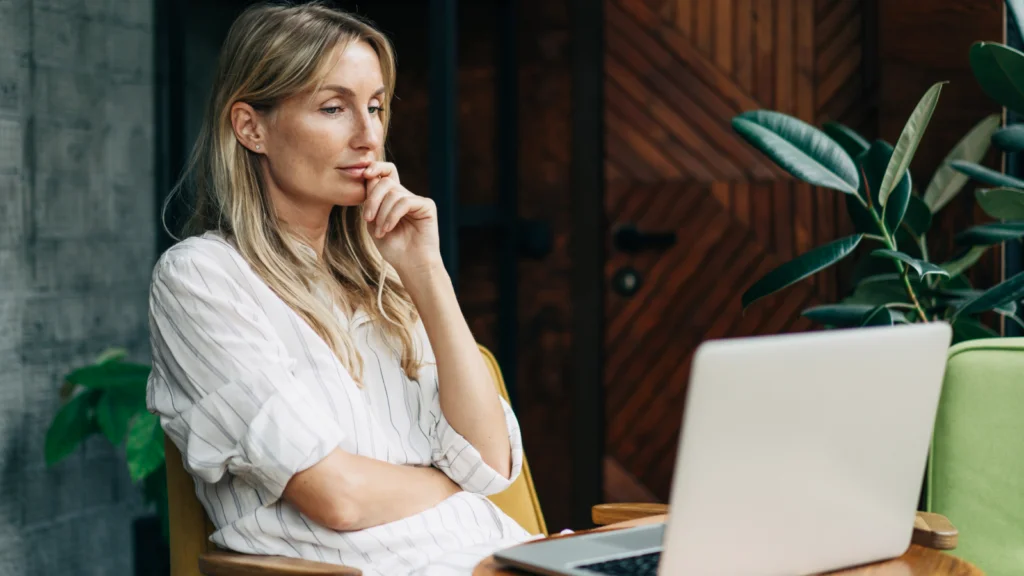 TikTok features and metrics to watch A woman with long blonde hair, wearing a striped shirt, looks at a laptop. Seated indoors with a potted plant and wooden decor.