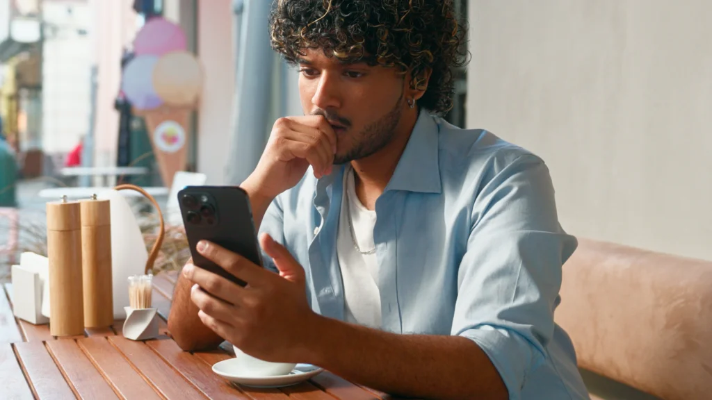 Understanding SPS PR and PSS A man with curly hair is sitting in a cafe, looking at his phone, and being focused.