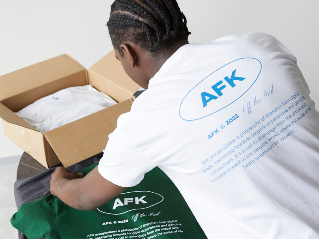 A backshot of a man in a white “AFK” t-shirt, lying out t-shirts on a table.