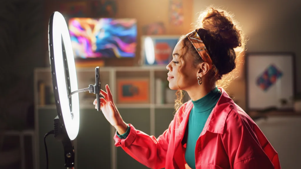 A woman is preparing to film herself using a smartphone on a tripod with a ring light.