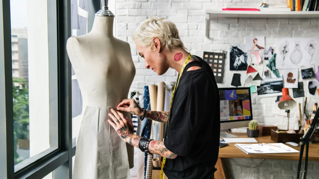 How to choose the right clothing niche for your brand A woman is sewing a dress in a well-lit studio, surrounded by fabric and sewing tools.