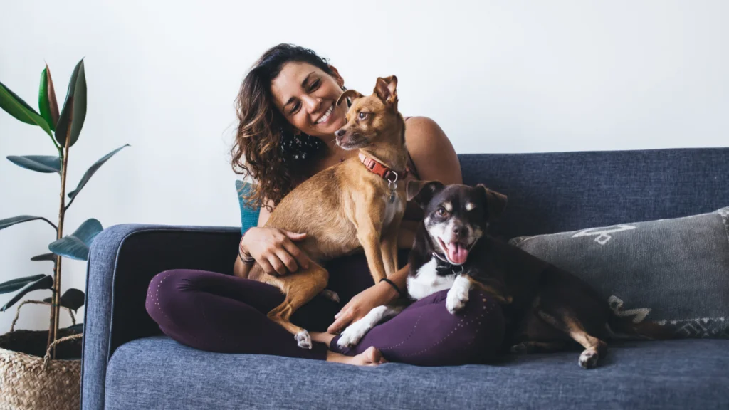 Pet owner apparel A woman sits on a couch, smiling, with two dogs resting beside her.