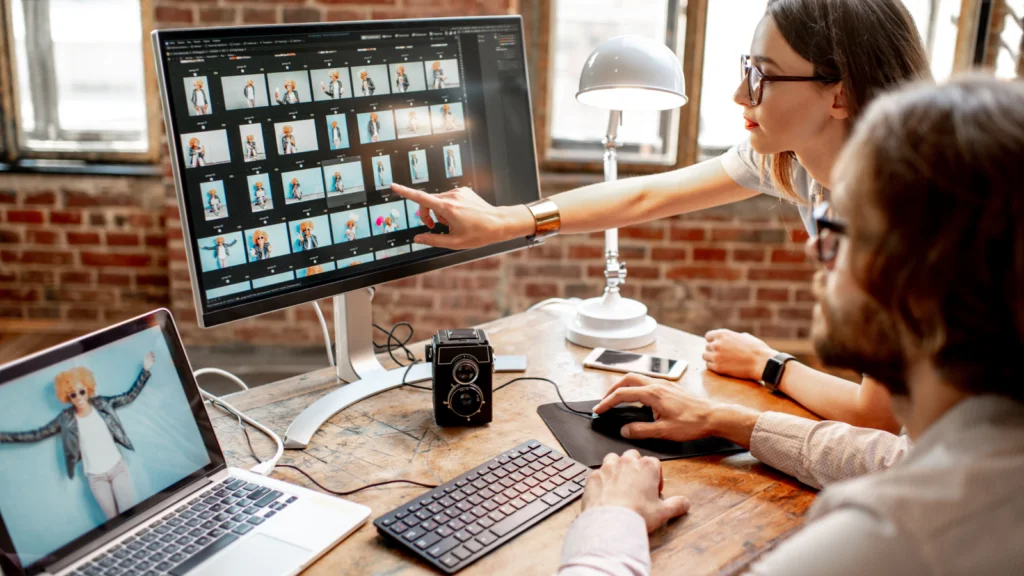 A woman and a man review photos on a computer in a brick-walled office.