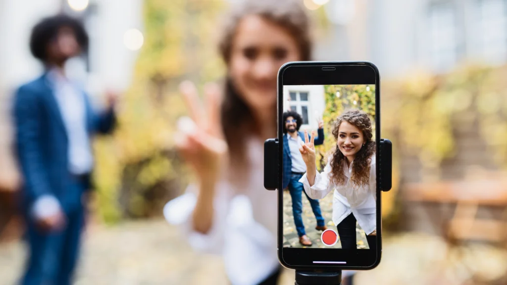 What to check when your samples arrive A woman smiling, flashing a peace sign in focus on a smartphone screen, with a blurred background of a man and autumn leaves, creating a cheerful ambiance.